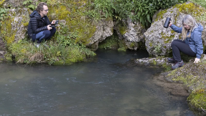 Dos personas junto al nacimiento del Ebro en Fontibre, grabando y recogiendo agua